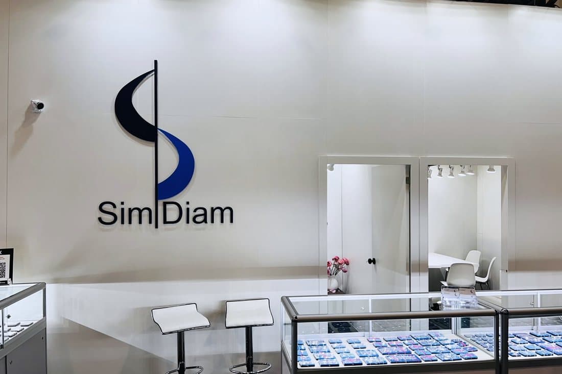 The Sim Diam booth at JCK Las Vegas: the S mark on a white wall above a lit diamond showcase